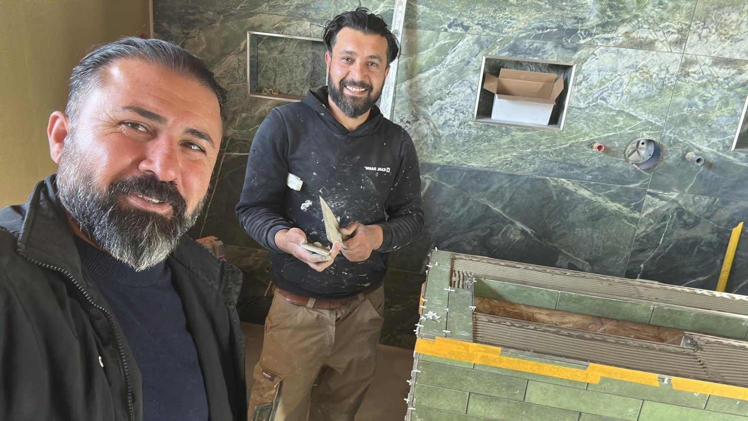 Faysal Maai und ein Mitarbeiter bei Fliesenarbeiten auf der Baustelle